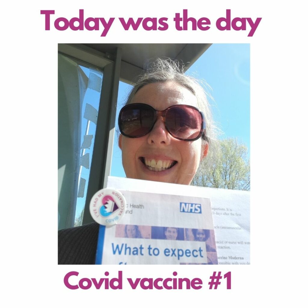A photo of me wearing sunglasses on a sunny day and holding up my covid vaccine sticker and NHS leaflet