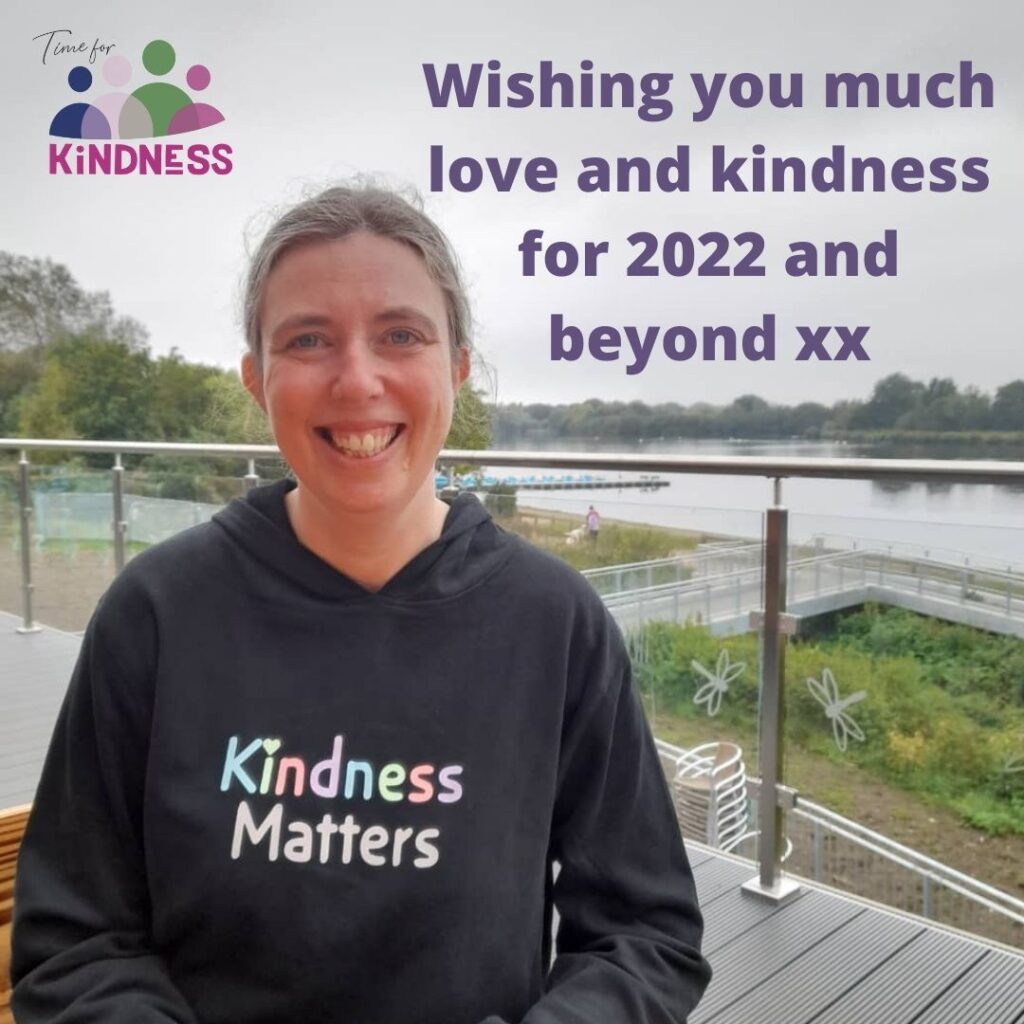 Sarah wearing a hoodie with "kindness matters" written on it. She is smiling broadly, a large lake behind her. Text reads "Wishing you much love and kindness for 2022 and beyond"
