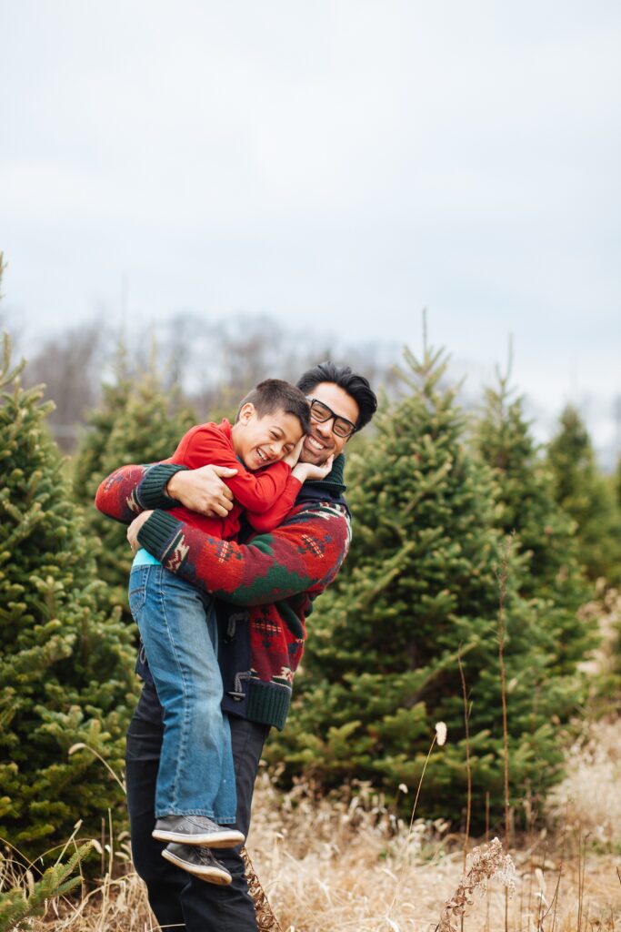 a man hugging a child in a field of Christmas trees