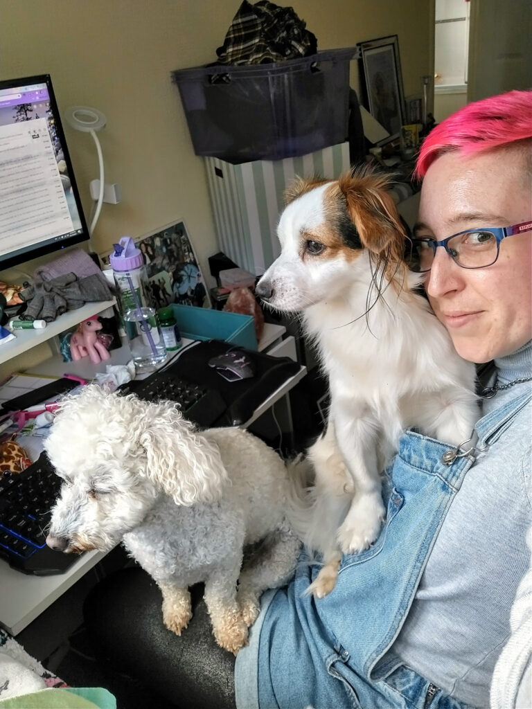 Alexis sits at her desk with 2 small dogs on her lap.