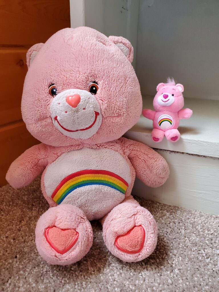 A large pink Care Bear and a small pink Care Bear sit on steps beside each other.