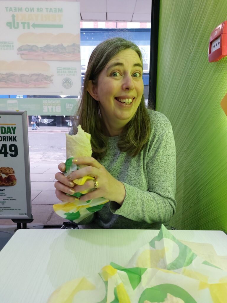 Sarah holding a Subway lunch wrap and smiling at the camera in a silly way