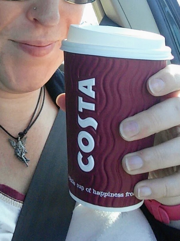 close up of a disposable Costa coffee cup being held by a woman wearing a fairy necklace with a nose piercing.