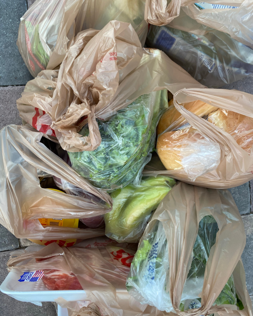 A selection of plastic bags with various foods in them including salad, bread, bananas and meat.