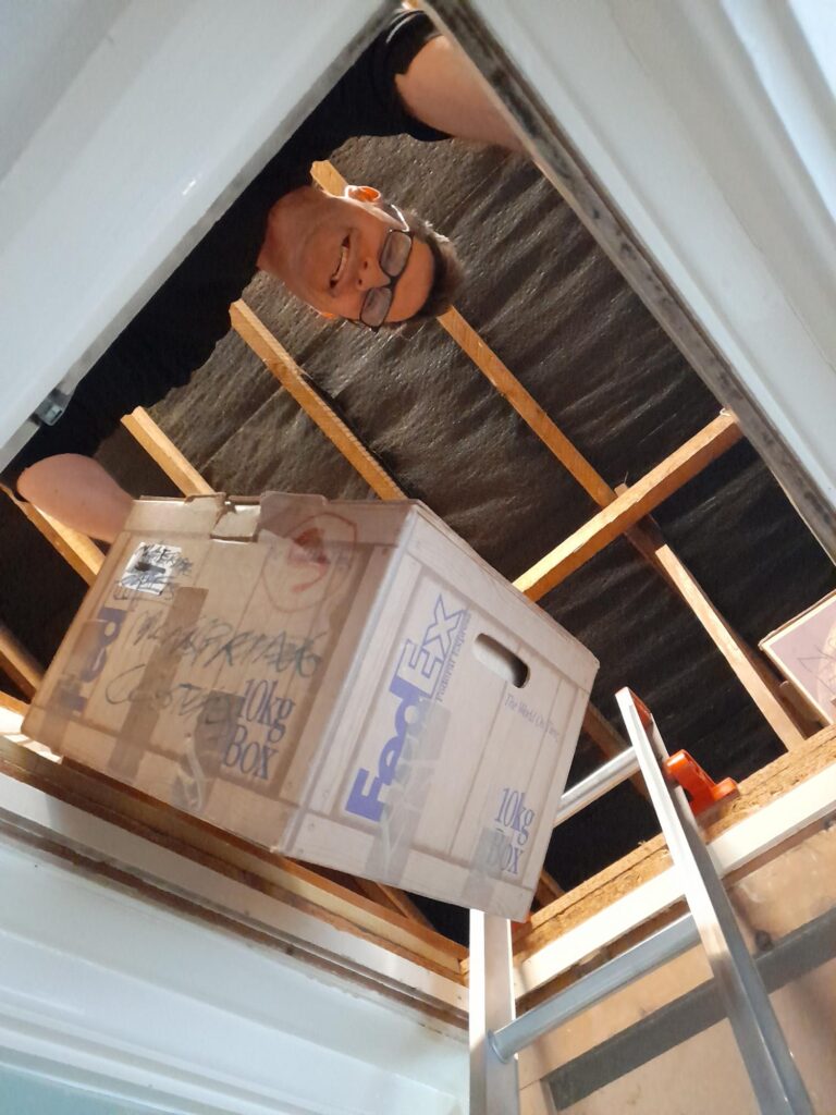 a man peeking out of a loft passing a FedEx box down.