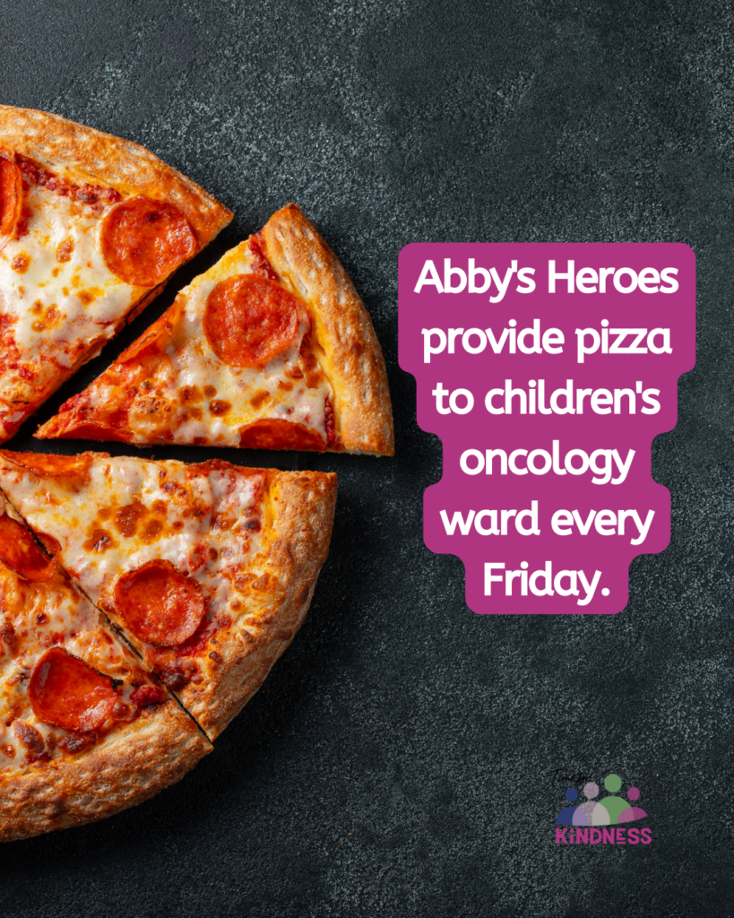 A pepperoni pizza on a black table, half of it visible on the left side of the image. To the right text reads “Abby's Heroes provide pizza to children's oncology ward every Friday.”