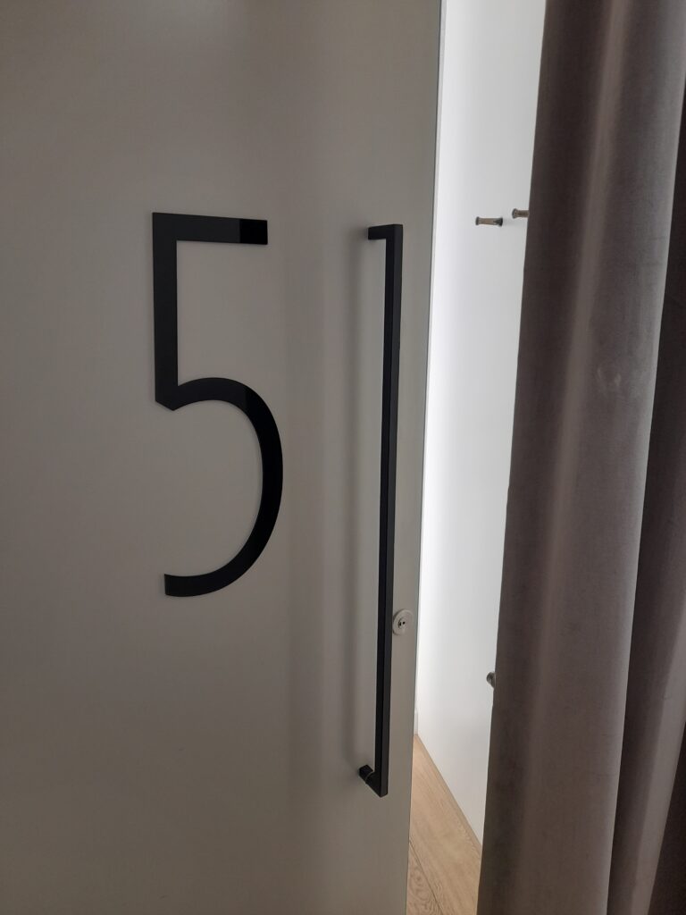 The door to a changing room cubicle slightly open. The number 5 is on the door beside a large handle.