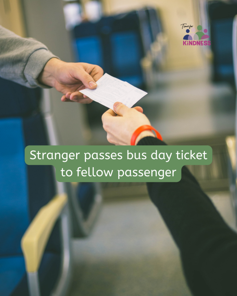 A hand passing a bus ticket to another hand on a bus. text overlaid reads “Stranger passes bus day ticket to fellow passenger.”