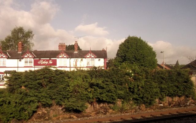 The Railway Inn in Rhosddu, a large white building, stands behind some trees along the railway from which the photo is being taken.
