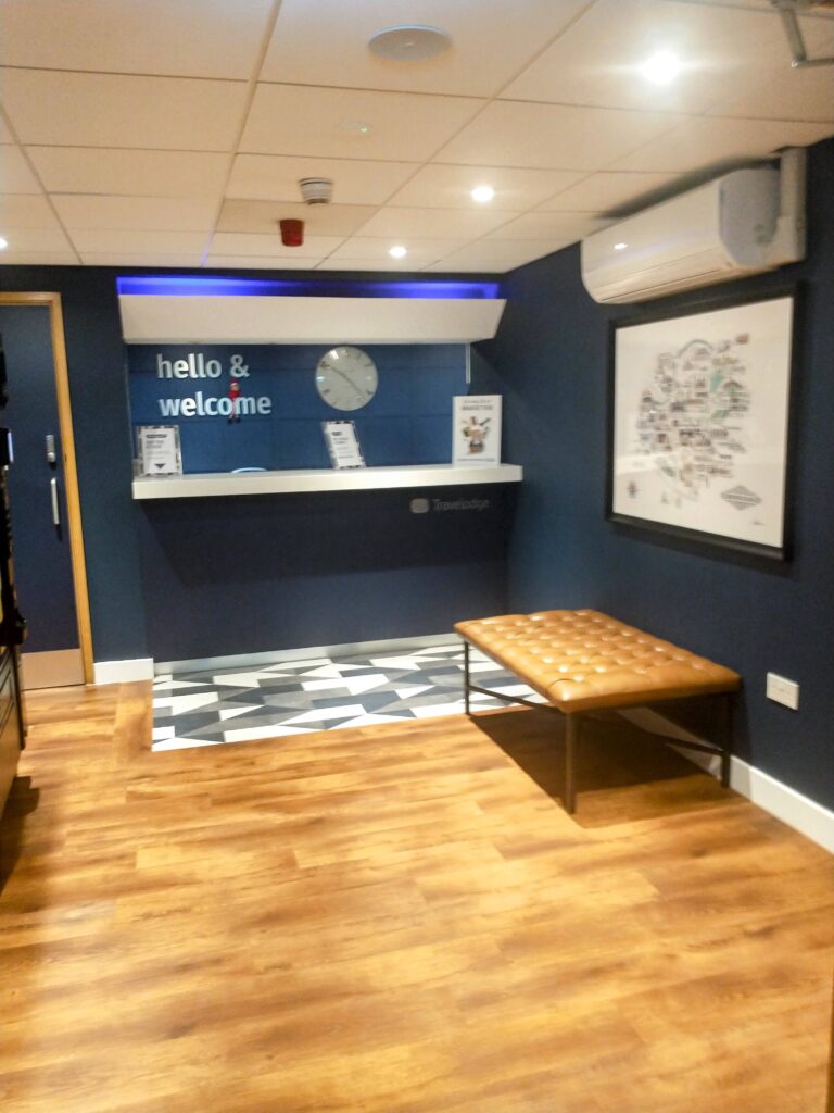 a Travelodge reception area with an elf sat on the “hello and welcome” sign.