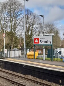 A train station platform with a large sign saying it’s Bramley station. The sky is blue behind some darkening grey clouds.