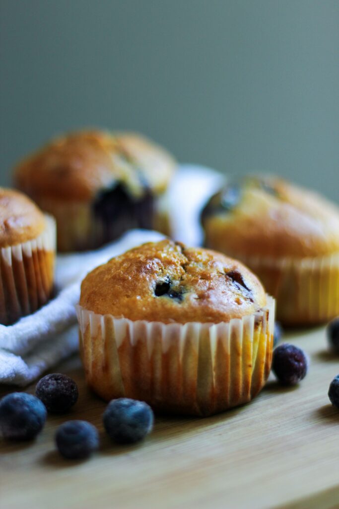 some blueberry muffins on a wooden table with blueberries scattered around them.