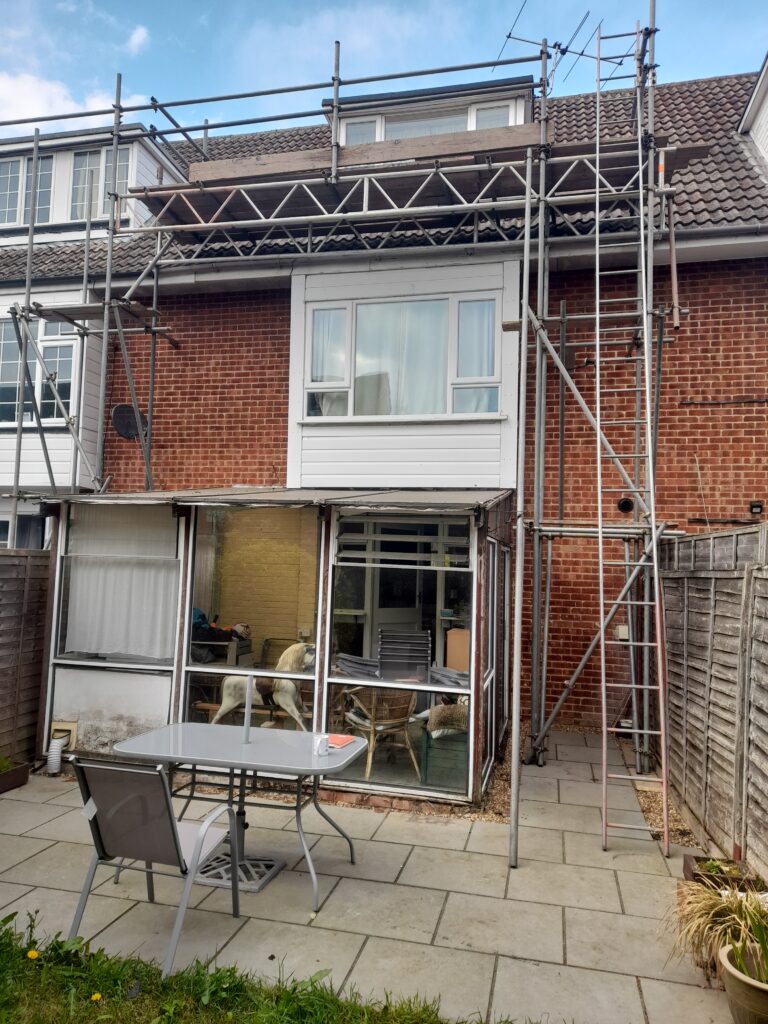 The back of a red brick townhouse with a conservatory, with scaffolding around it up to the roof.