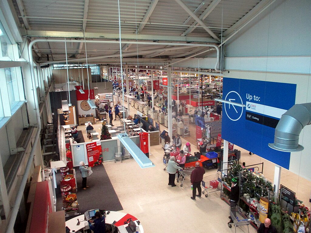 a view down into a Tesco supermarket. Rows of checkouts along the right and customer service in the middle with people milling around everywhere.