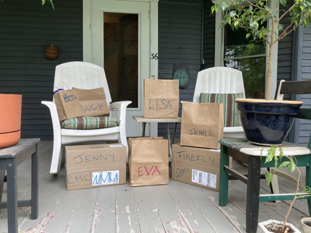 a front porch with five bags and two larger boxes which all have people's names written on them in big block letters. The bags contain COVID tests.
