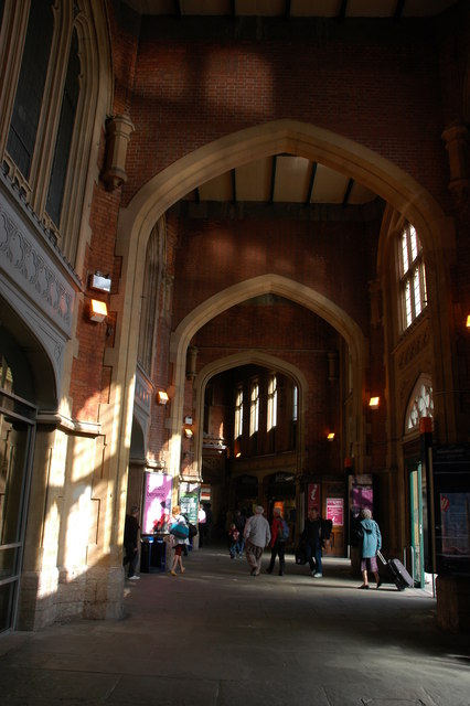 Large brick archways into Bristol Temple Meads station. People of various ages are walking into the station, some pulling suitcases.