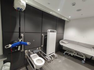 A large disabled toilet with a changing space, the red pull cord all the way to the floor, and a hoist.