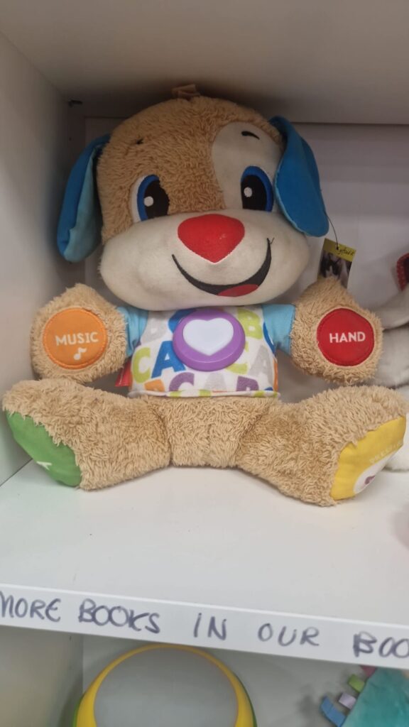 A teddy with brown fur, blue ears and on each paw a yellow, red, green or yellow patch. The two visible on the arms say “music” and “hand.”