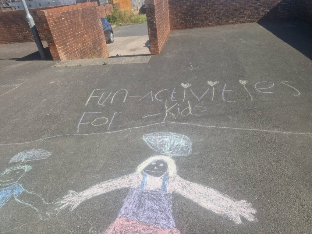 The words “fun activities for kids” written in chalk on tarmac. Beneath them are chalk drawings of children holding hands and talking to each other.