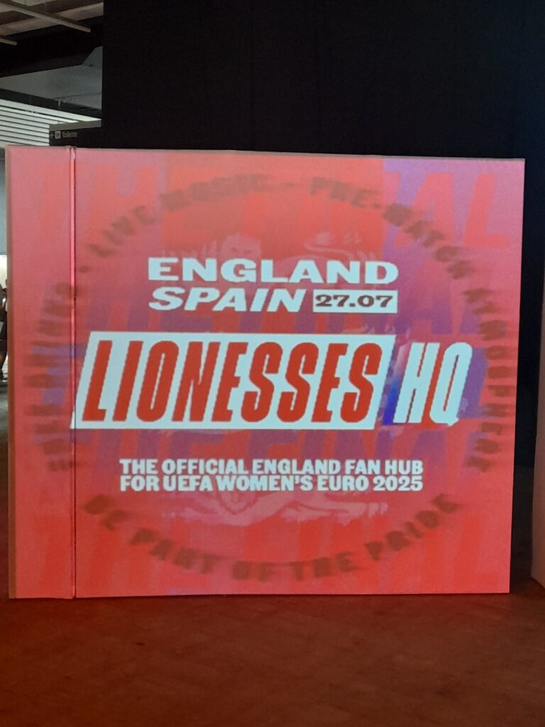 A large red sign reading "England Spain 27. 07. Lionesses HQ. The official England fan hub for UEFA Women's Euro 2025.”