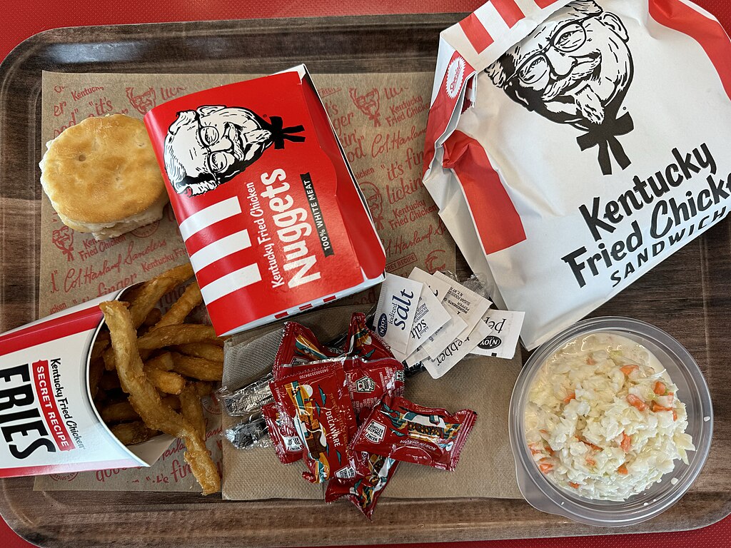 a tray with a selection of goodies from KFC on it including a sandwich, nuggets, fries, coleslaw, a scone and some salt and sauces.