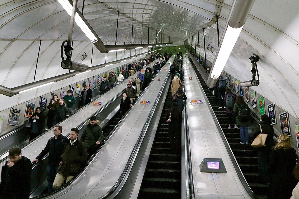 two up and two down escalators at Holborn tube station. There are lots of people on each and they are both quite long going up quite high from the station platform.