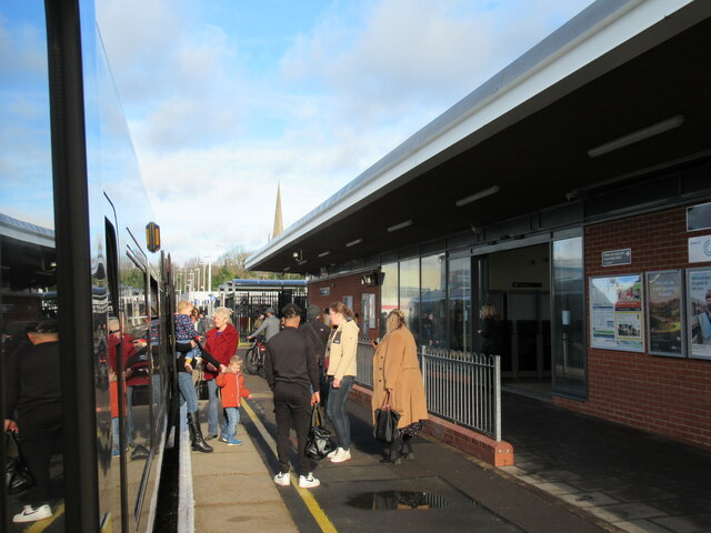 A platform at Wokingham train station with a train pulled up and people getting on and off it.