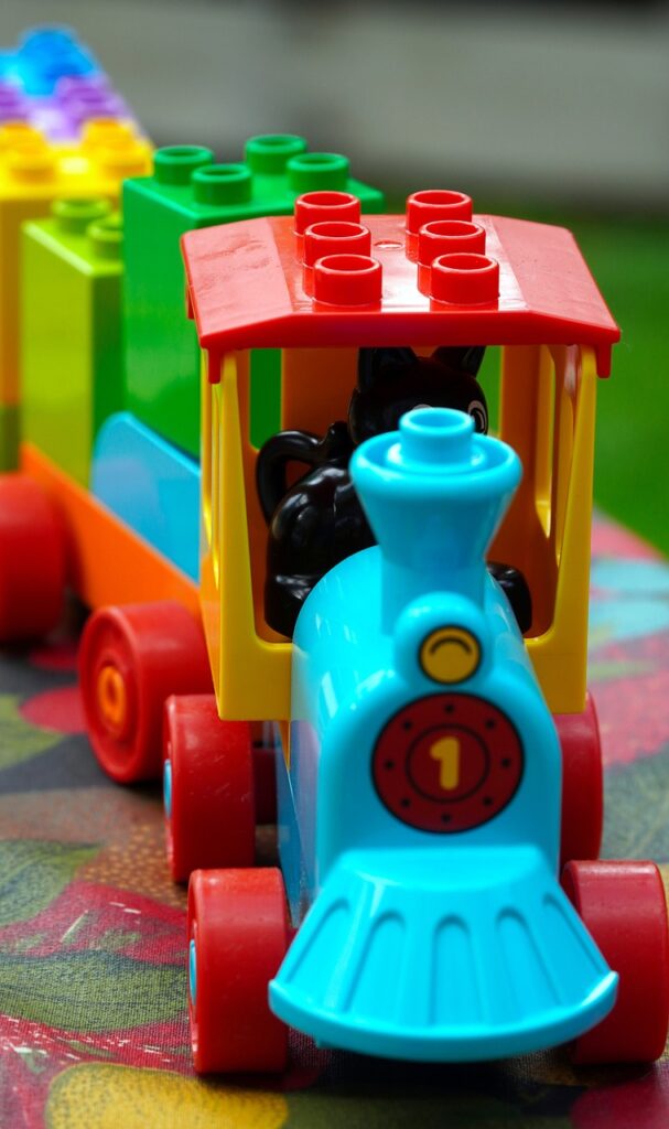 a close up of a toy train with a light blue engine, red wheels, and alternating yellow, green, blue and purple carriages.