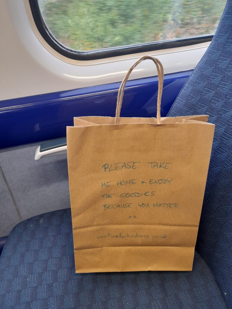A brown paper bag sitting on a train seat with the words “please take me home and enjoy the goodies because you matter” written on it.