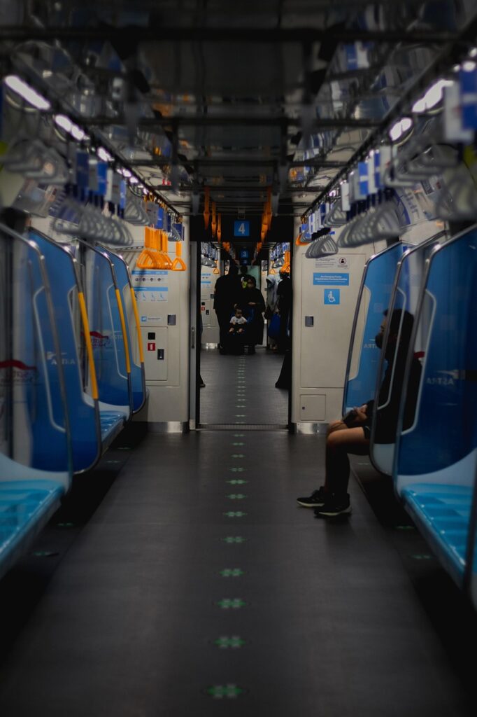 A view down a train carriage with one person sat to the right and a family with toddler standing in the aisle further down.