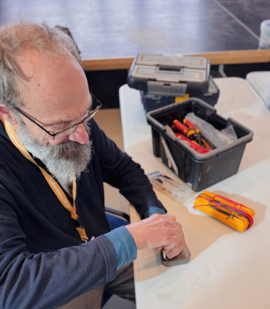 One of the volunteers at the Aberystwyth repair cafe sits at a bench as he uses a screw driver to fix a small item