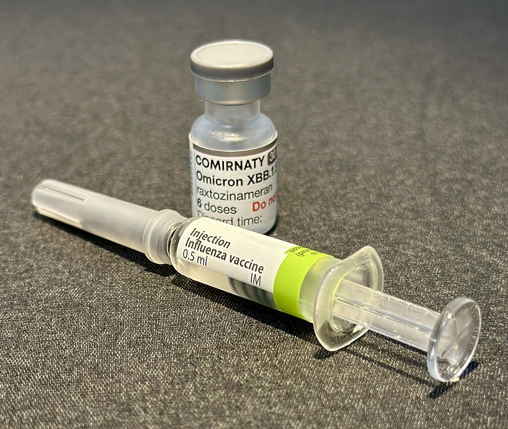 a covered vaccination needle with a label on it reading injection, influenza vaccination, beside a pot with a comirnaty omicron label on it.