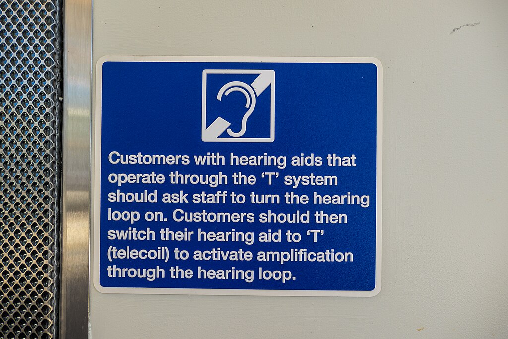 A blue hearing loop sign on a train which reads customers with hearing aids that operate through the T system should ask staff to turn the hearing loop on. Customers should then switch their hearing aid to T (telecoil) to activate amplification through the hearing loop.