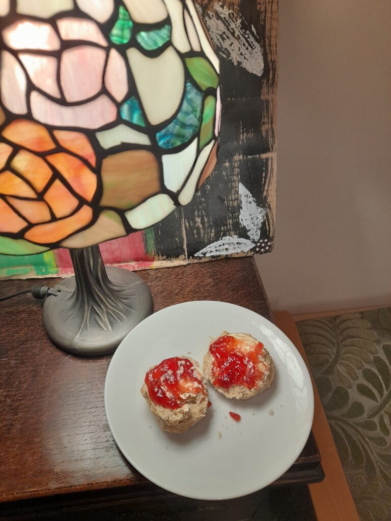 a scone with a red jam on it sitting on a plate on a table by a light.