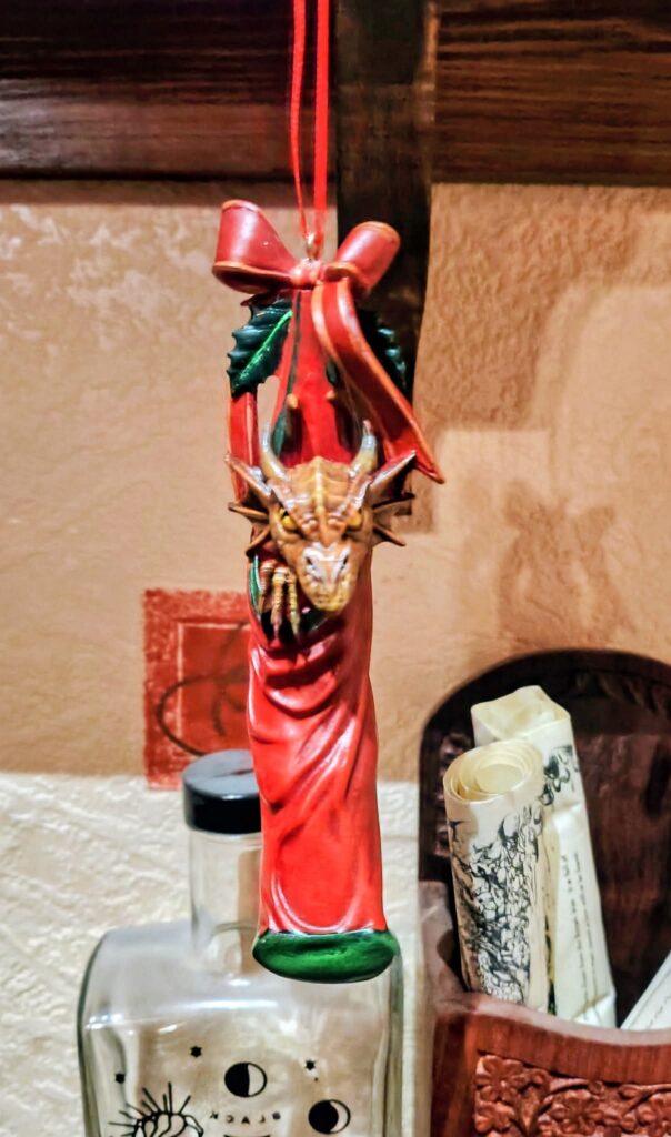 a hanging Christmas decoration of a dragon in a red stocking with a bow and holly above it.