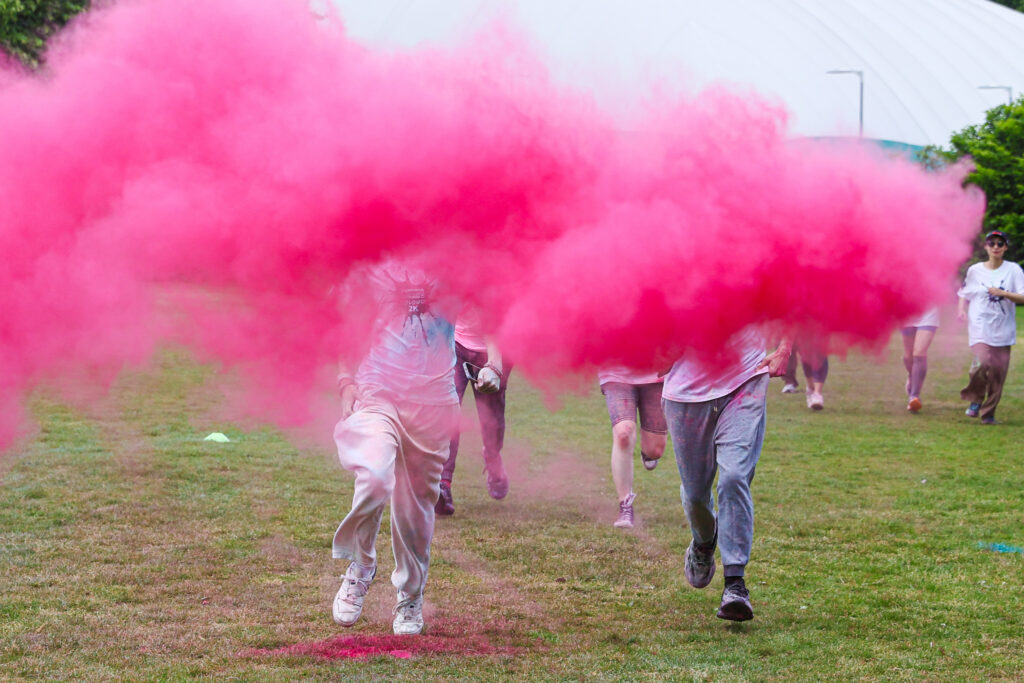 four people running towards the camera obscured by a poof of thick red mist which hides their heads.