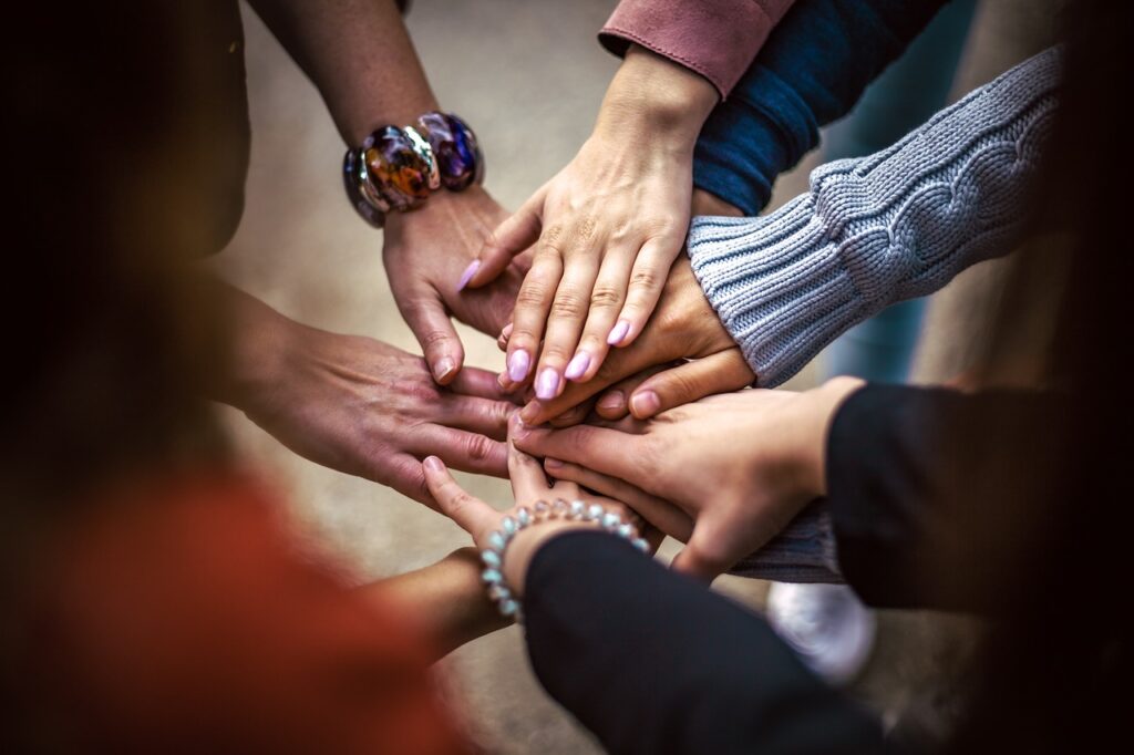 A group of hands on top of each other coming from people stood around in a circle.