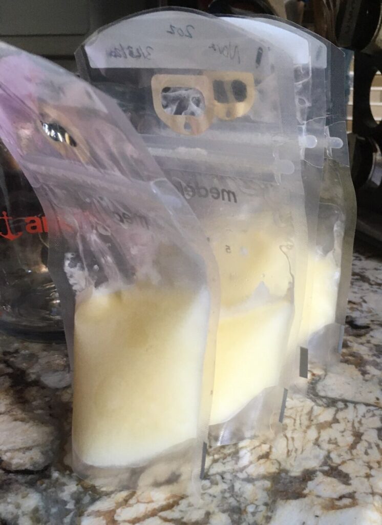 three plastic bag storage containers of breast milk, zip locked and labelled with date.