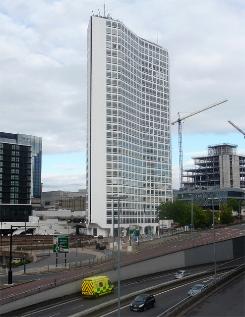 a dual carriageway road in the foreground which goes into a tunnel with other roads beyond it going around a white skyscraper that reaches into a grey Birmingham sky.