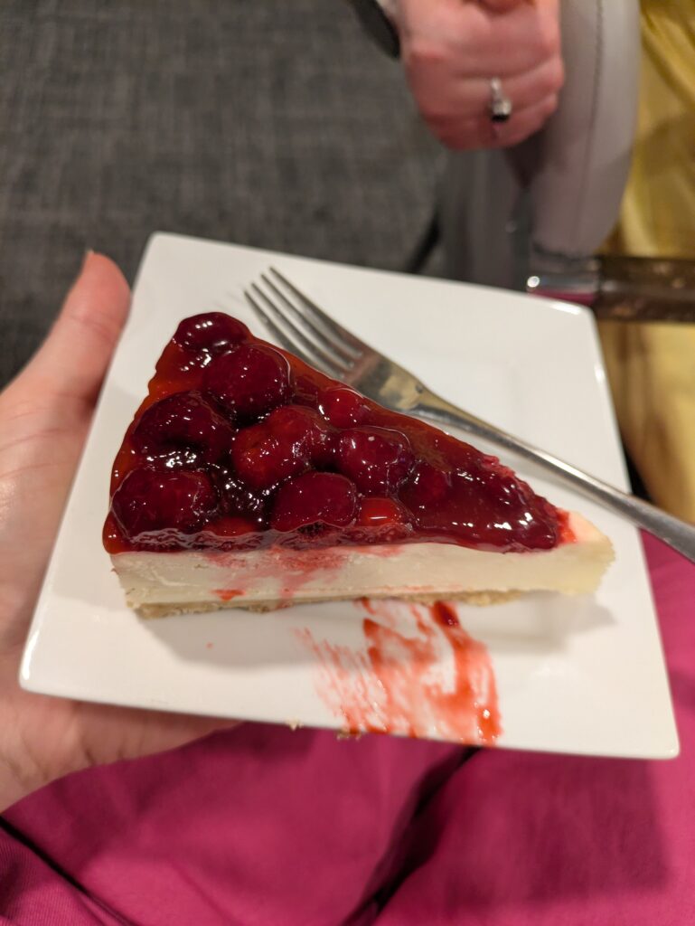 a delicious looking cheesecake topped with red berries and coulis on a square white plate.