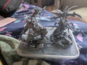 two grey 3d printed models. One seems to be a tiger wearing martial arts outfit and pulling a martial arts pose, the other is a beetle style monster with wings and several skinny legs.