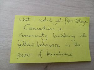 A hand-written yellow post-it note that says What I want to get from today: Connection and community building with fellow believers in the power of kindness